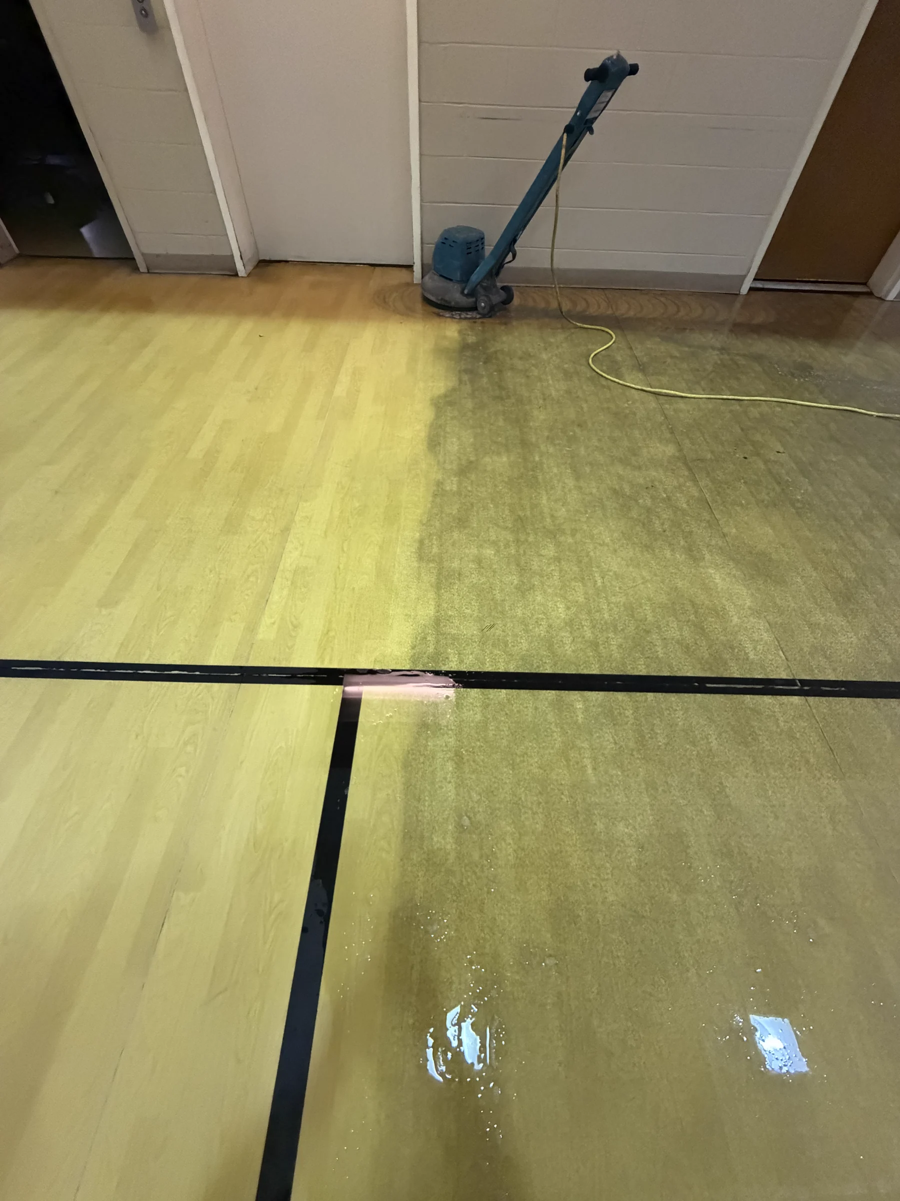 Commercial hardwood gym floor during cleaning, with the cleaned area visible beside the untreated floor