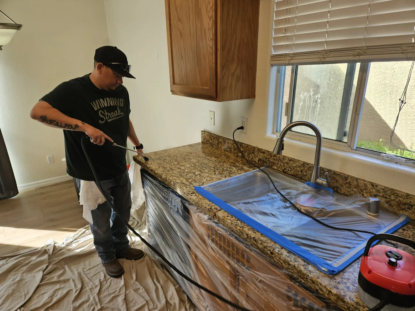 Technician cleaning a protected granite countertop beside a kitchen sink