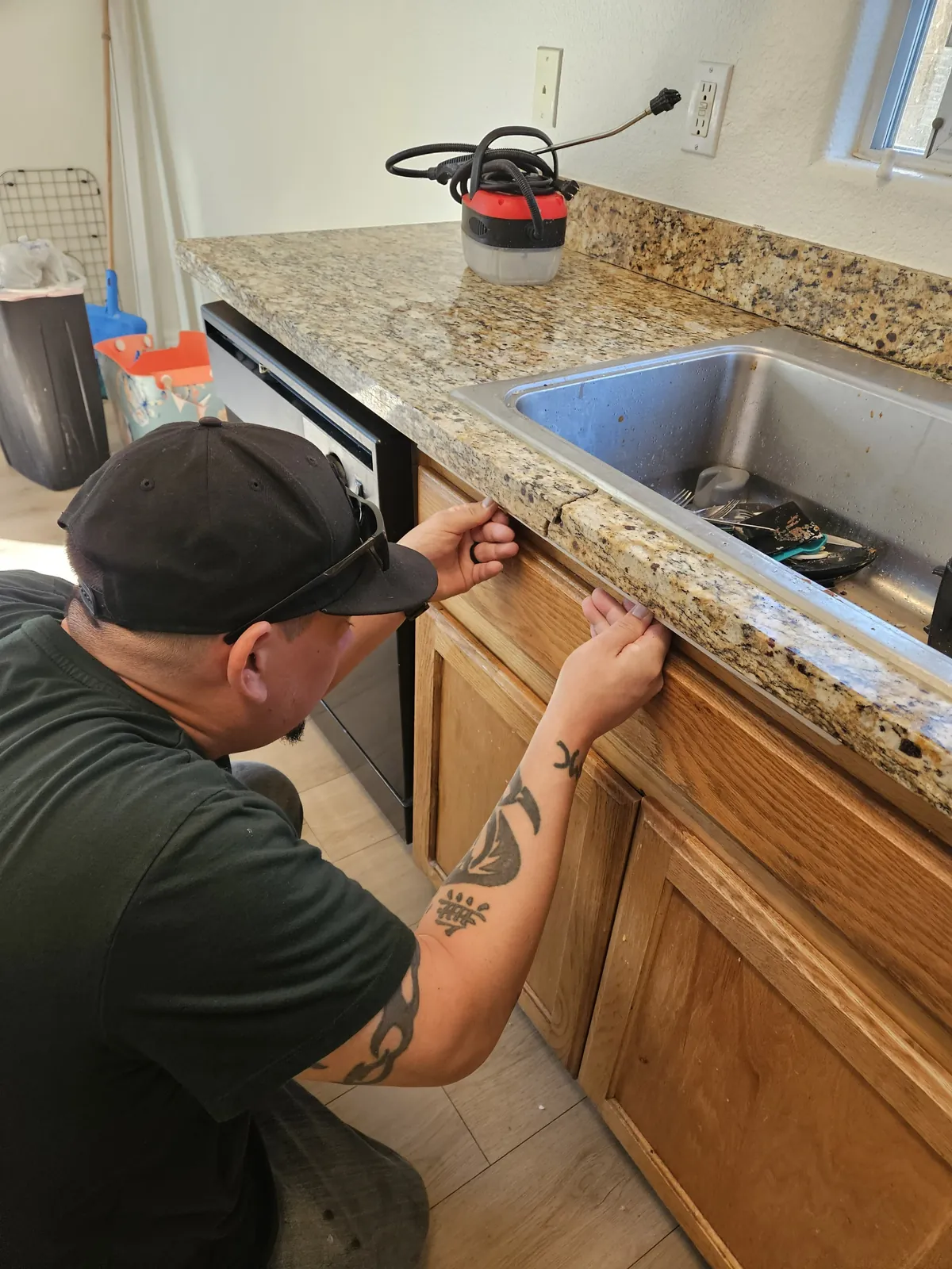 Technician inspecting a damaged granite edge beside a kitchen sink