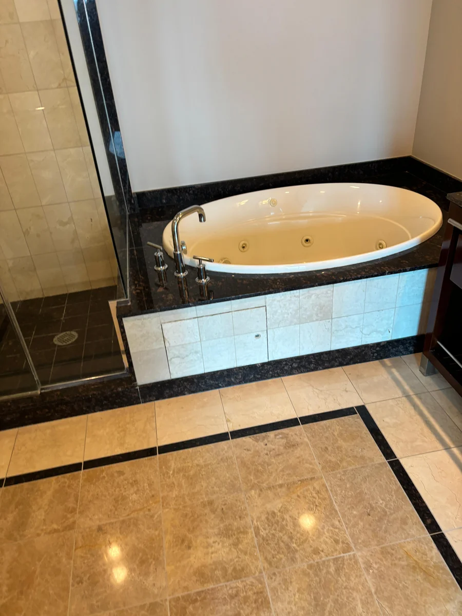 Restored marble bathroom floor beside a dark stone tub deck