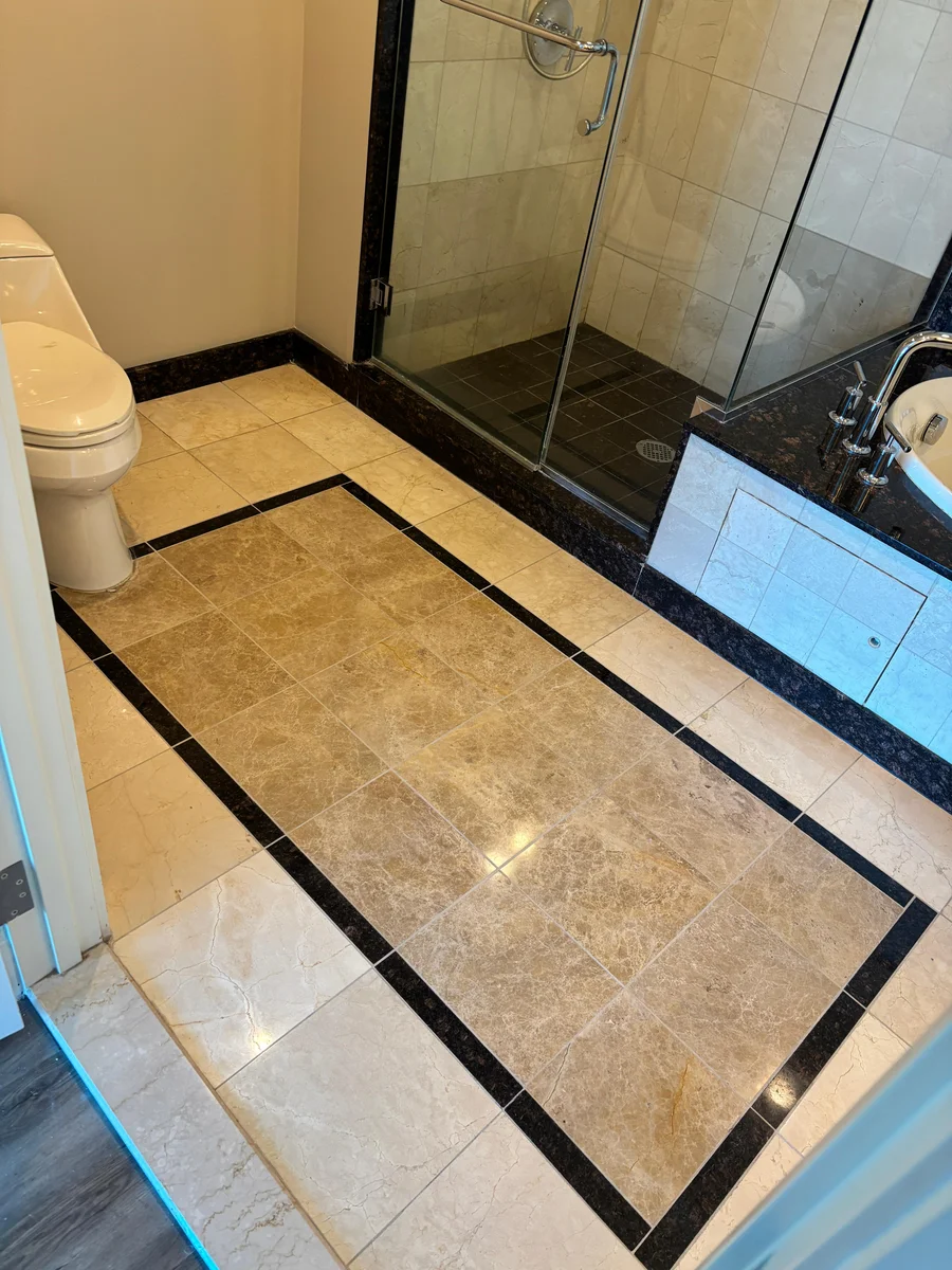 Finished marble tile bathroom floor framed by a dark granite border